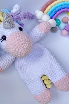 a crocheted stuffed unicorn laying next to a rainbow toy