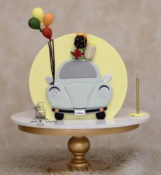 a birthday cake with a vw bug on top and balloons in the air above it