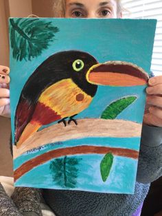 a woman holding up a painting of a toucan bird on a tree branch