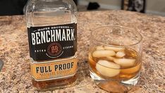 a bottle of benghmark full proof whiskey next to a glass filled with ice cubes