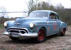 an old blue car parked on top of a dirt field