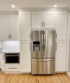 a silver refrigerator freezer sitting inside of a kitchen next to white cabinets and wooden floors