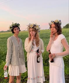 three women in white dresses standing next to each other holding bottles and looking at the camera