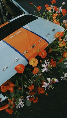 an orange and blue surfboard sitting on the side of a car with flowers around it