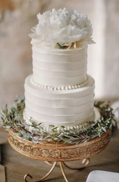 a wedding cake with white flowers and greenery sits on a gold plated stand