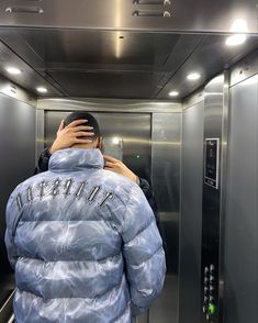 a person in a blue jacket taking a selfie with his cell phone while standing inside an elevator