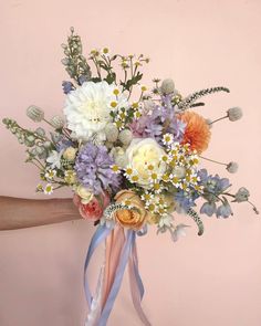 a bouquet of flowers is being held by someone's hand on a pink background