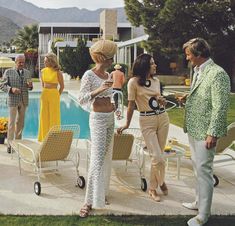 three women and two men standing near a pool talking to each other in front of some lawn chairs