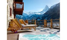 a hot tub sitting on top of a wooden deck next to a mountain covered in snow