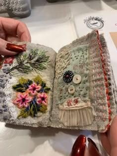 a woman is holding an open book with buttons and flowers on it, in front of other handmade items