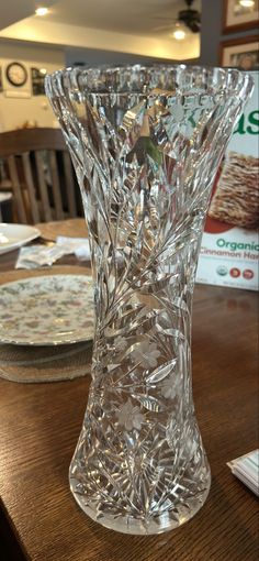 a glass vase sitting on top of a wooden table next to plates and napkins