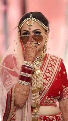 a woman in a red and gold bridal outfit holding her hand up to her face