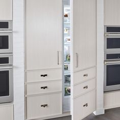 an open refrigerator and two ovens in a room with white walls, doors opened to reveal the kitchen