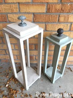 two small white wooden lanterns sitting next to each other on the ground near a brick wall