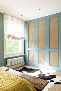 a bedroom with blue walls and white carpeted flooring next to a bed in front of a window