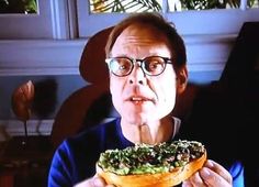 a man with glasses is eating a doughnut covered in greens and other toppings