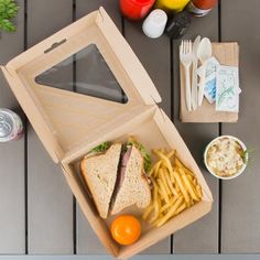 a sandwich and french fries in a cardboard box on a wooden table next to drinks