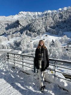 a woman standing on top of a snow covered slope next to a wooden fence and mountains