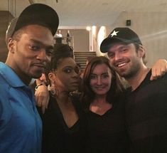 four people posing for a photo in front of some stairs with one person wearing a hat