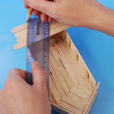 a person is holding a ruler in front of a wooden box with a house on it