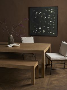 a wooden table with two white chairs and a vase on the wall next to it