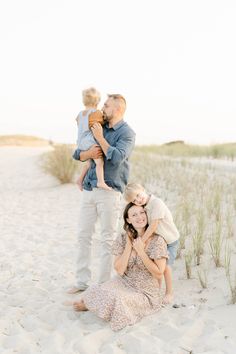 a family poses on the beach in front of some tall grass and sand dunes at sunset