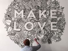 a man is drawing on the wall with flowers and words that spell out make love