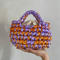 a hand holding an orange and purple purse with braiding on it's sides