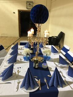 a table set up with blue napkins, silverware and candles for an event