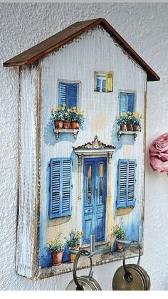 a house with blue shutters is hanging on the wall next to two key holders