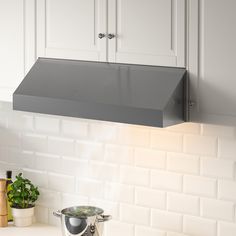 a stove top oven sitting next to a pot on a kitchen counter with white cabinets