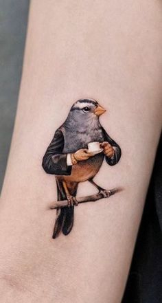 a small bird tattoo on the arm with a cup in it's beak and an arrow