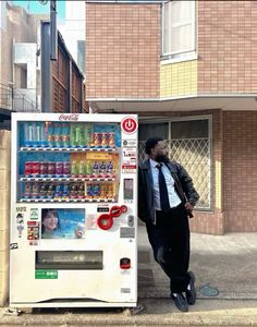 a man standing next to a vending machine on the side of a road in front of a building