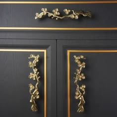 a black cabinet with gold trimming and flowers on the door handles, along with two matching drawer pulls