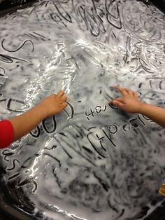 two children reaching out their hands to touch the bottom of a large metal pan with writing on it