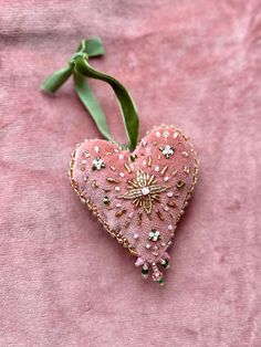 a pink heart shaped ornament hanging from a green ribbon on a pink background