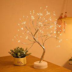 a small tree with white lights on top of a wooden table next to a potted plant