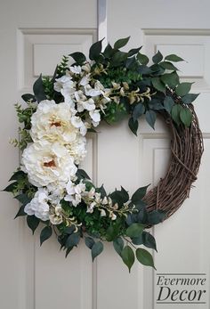 a wreath with white flowers and greenery hangs on a door