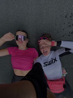 two women laying on the ground with their arms around each other and wearing sun glasses