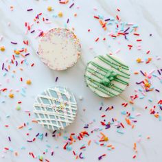 three decorated cookies sitting on top of a table covered in sprinkles