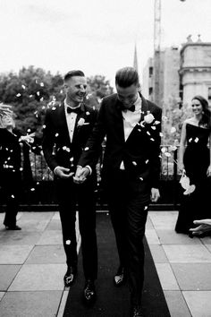 two men in tuxedos are walking down the street as confetti is thrown around them