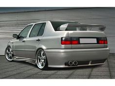 the rear end of a silver car parked in front of a garage door and wall