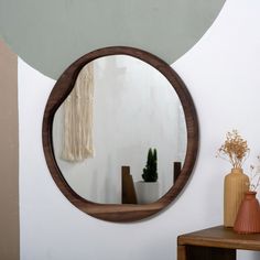 a round mirror hanging on the wall next to a table with vases and potted plants