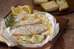 two fish fillets on a plate with bread and lemon wedges