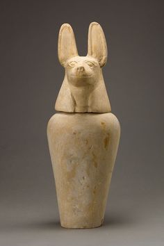 an ancient egyptian statue with ears on it's head is shown in front of a gray background