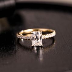 an engagement ring with a princess cut diamond surrounded by small white diamonds on a black surface