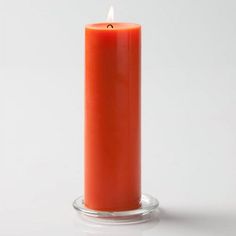 an orange candle is sitting on a glass stand with a white background in the foreground