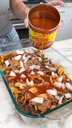 a person pouring sauce on food in a glass dish