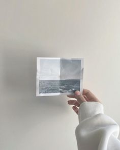 a person holding up an open polaroid with the ocean in the background and white walls