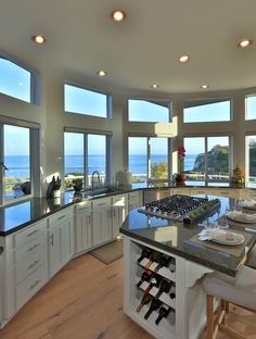 a large kitchen with an island and wine rack in the center, overlooking the ocean